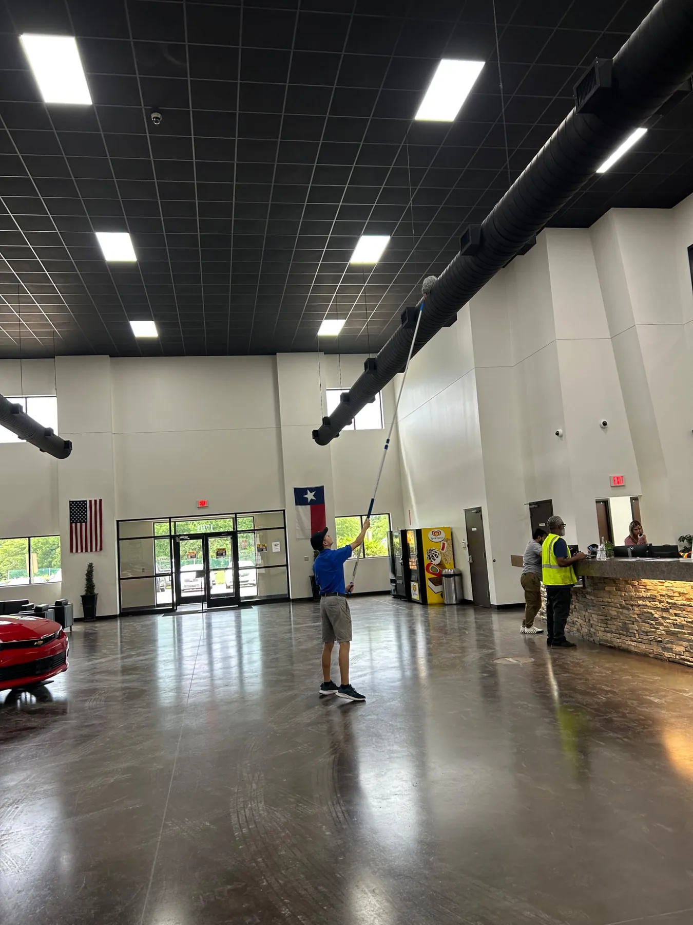 Brite-Way technician high dusting exposed ductwork inside a large commercial showroom